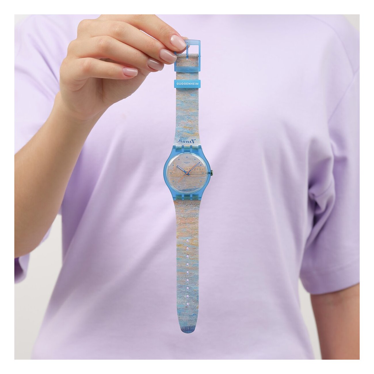 Eine Hand hält eine Swatch Unisexuhr aus Kunststoff. Das Zifferblatt und Armband sind hellblau mit gemalten Texturen.