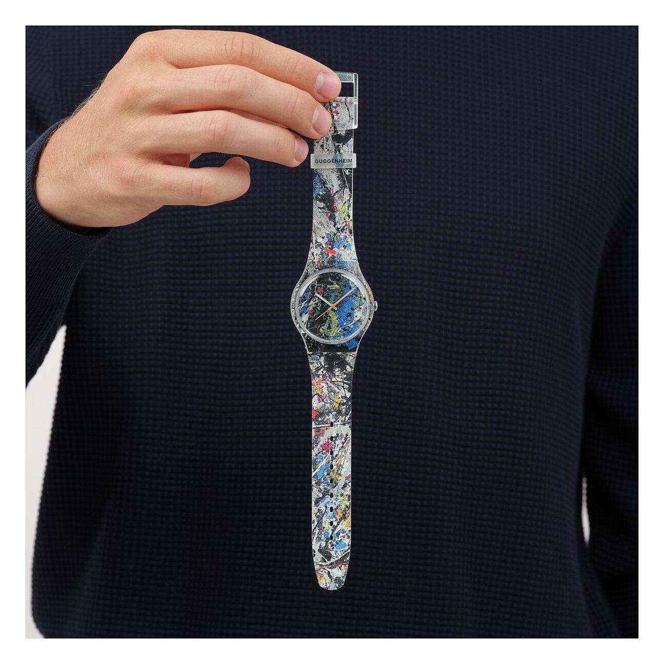 En mand holder et Swatch unisex-ur af plast med et farverigt stænkmønster i hånden.