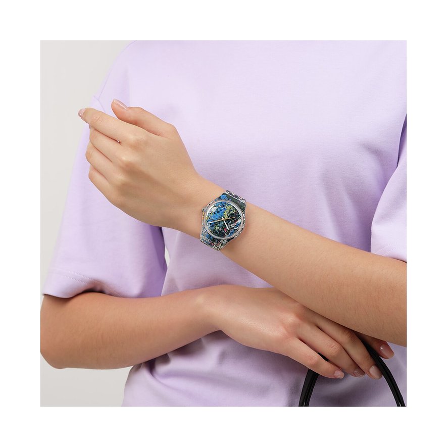 På håndleddet bæres et Swatch unisexur i plastik med et farverigt design, der forestiller en verdenskugle.