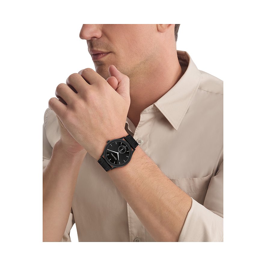 Nahaufnahme einer Calvin Klein Herrenuhr aus schwarzem Edelstahl am Handgelenk eines Mannes, der ein helles Hemd trägt.