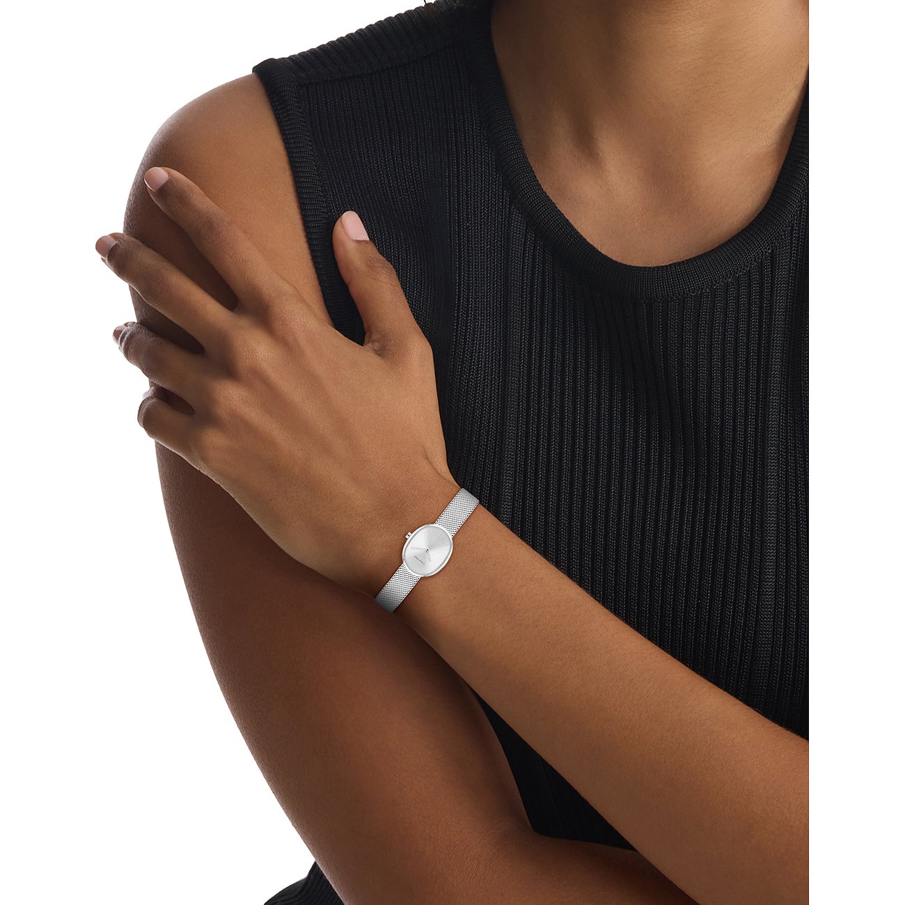 Am Arm einer Frau getragen: Calvin Klein Damenuhr aus Edelstahl mit ovalem Zifferblatt und Mesh-Armband.