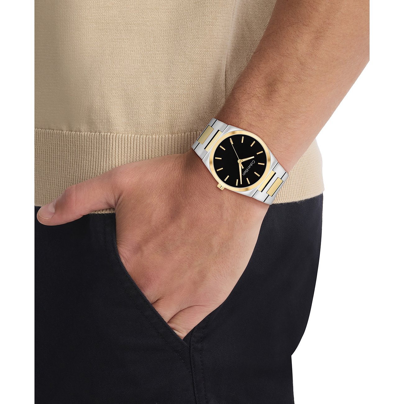 Am Handgelenk eines Mannes getragene Calvin Klein Herrenuhr aus gold- und silberfarbenem Edelstahl mit schwarzem Zifferblatt.