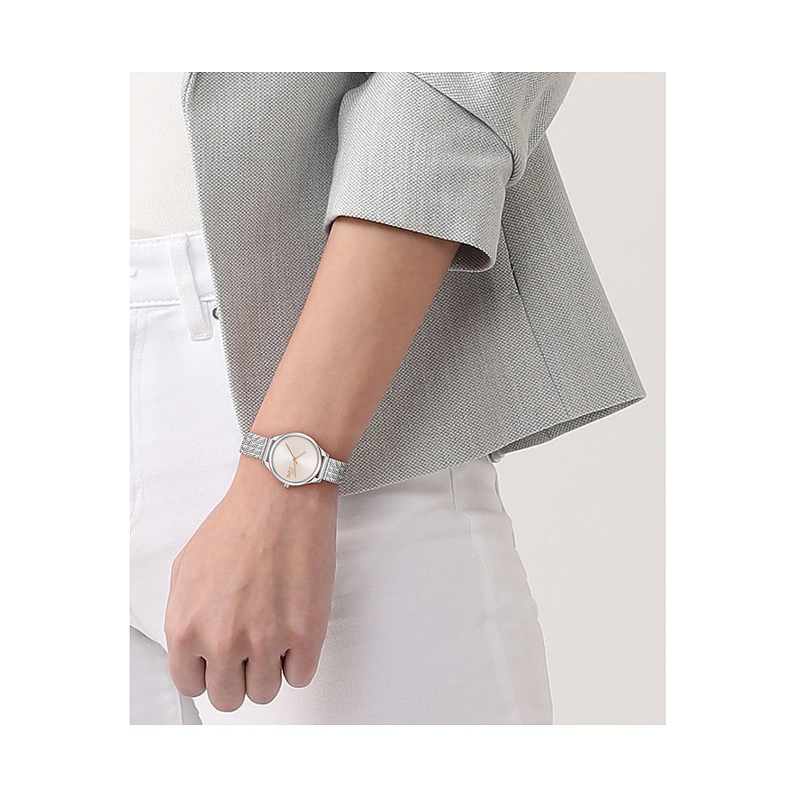 Nahaufnahme einer Lacoste Damenuhr aus Edelstahl mit silbernem Mesh-Armband und beigem Ziffernblatt am Handgelenk