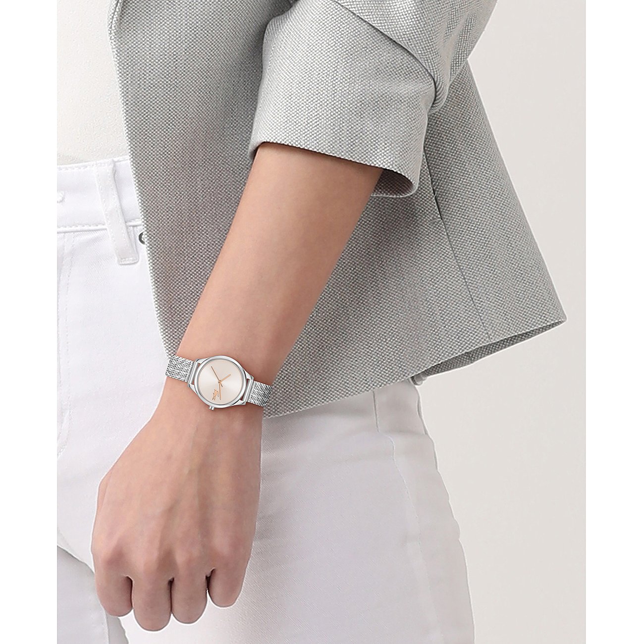 Nahaufnahme einer Lacoste Damenuhr aus Edelstahl mit silbernem Mesh-Armband und beigem Ziffernblatt am Handgelenk