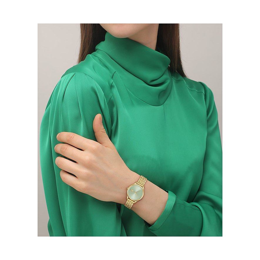 Eine Frau trägt eine goldfarbene Lacoste Damenuhr aus Edelstahl mit mintgrünem Zifferblatt und gemustertem Armband.
