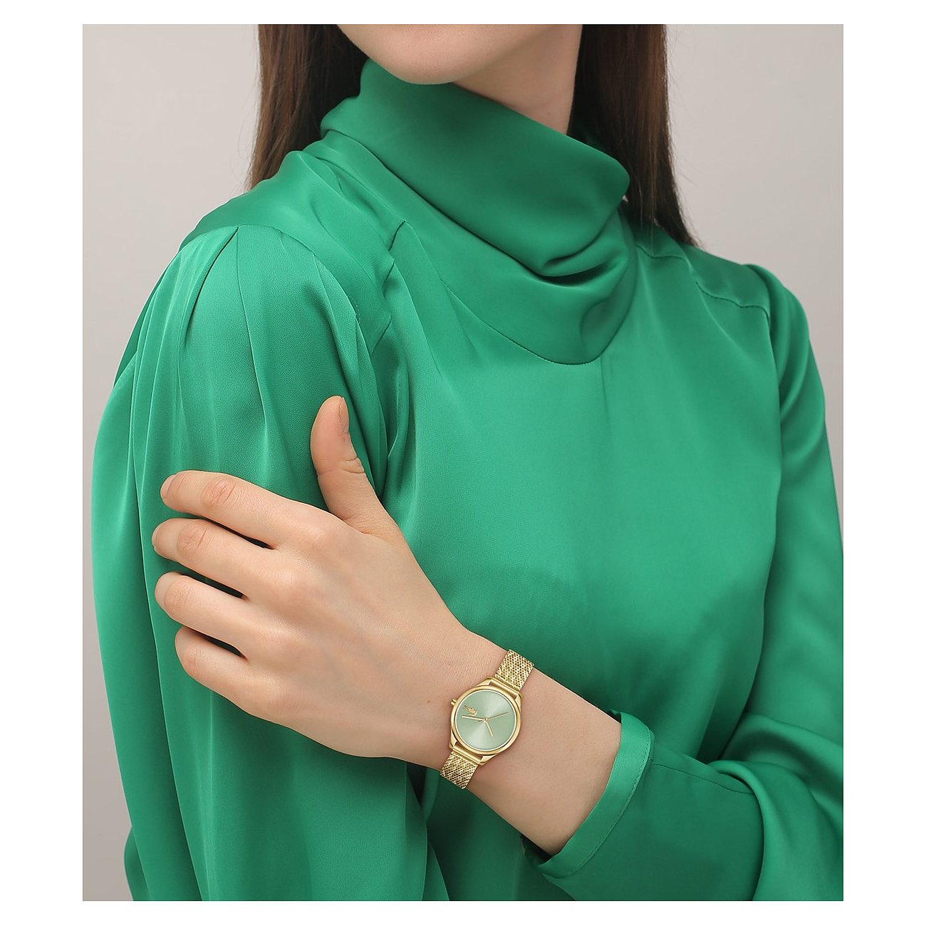 Eine Frau trägt eine goldfarbene Lacoste Damenuhr aus Edelstahl mit mintgrünem Zifferblatt und gemustertem Armband.