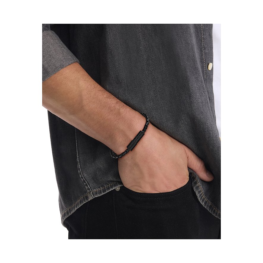 Ein Calvin Klein Armband aus schwarzem Edelstahl in Form eines dunklen Kettenarmbandes, auf einem Männerarm getragen.