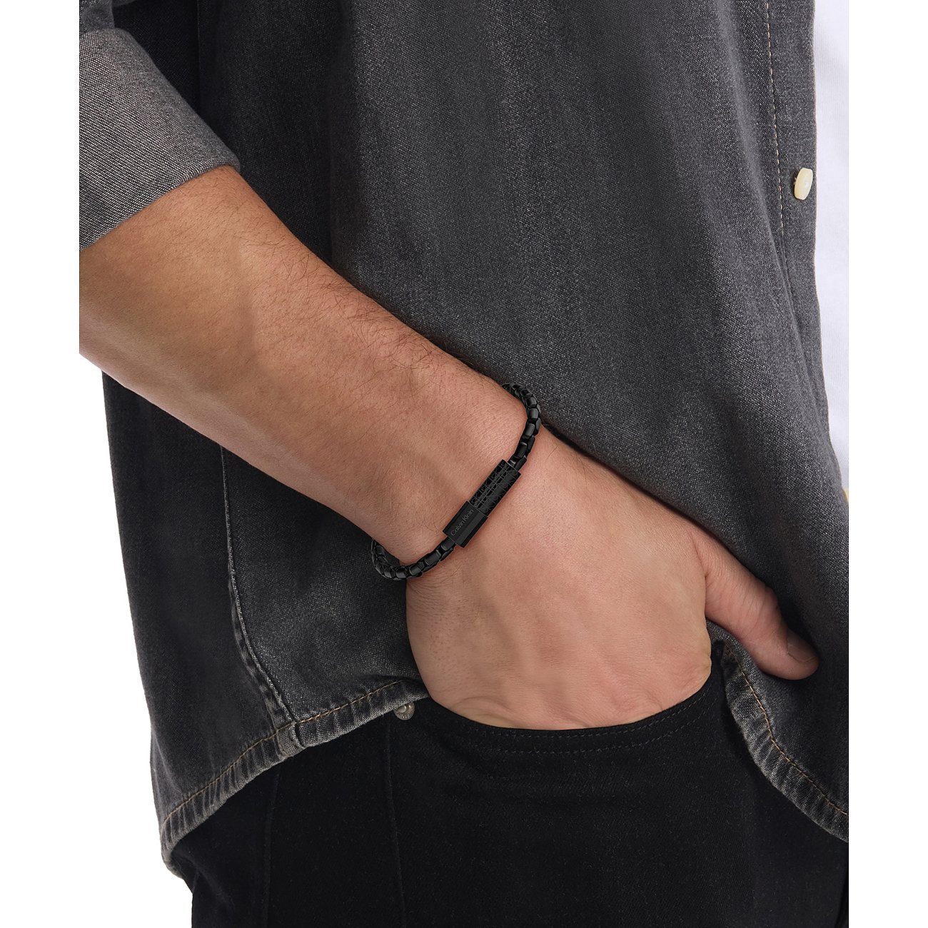 Ein Calvin Klein Armband aus schwarzem Edelstahl in Form eines dunklen Kettenarmbandes, auf einem Männerarm getragen.