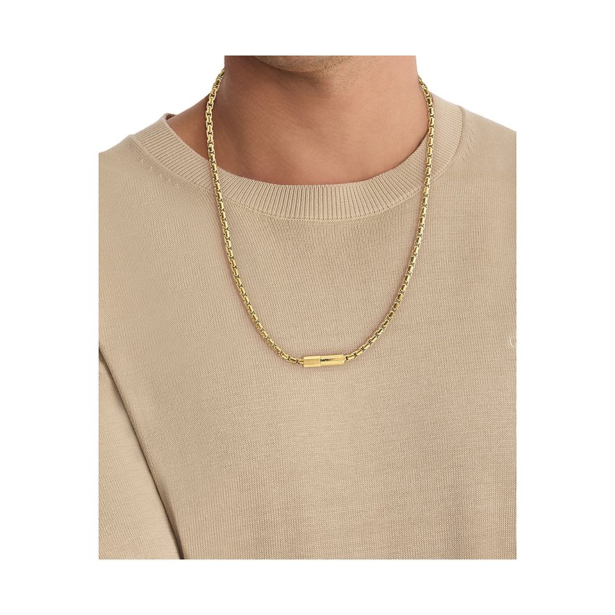 Een gouden Calvin Klein roestvrijstalen halsketting met cilindervormige hanger wordt gedragen door een man.