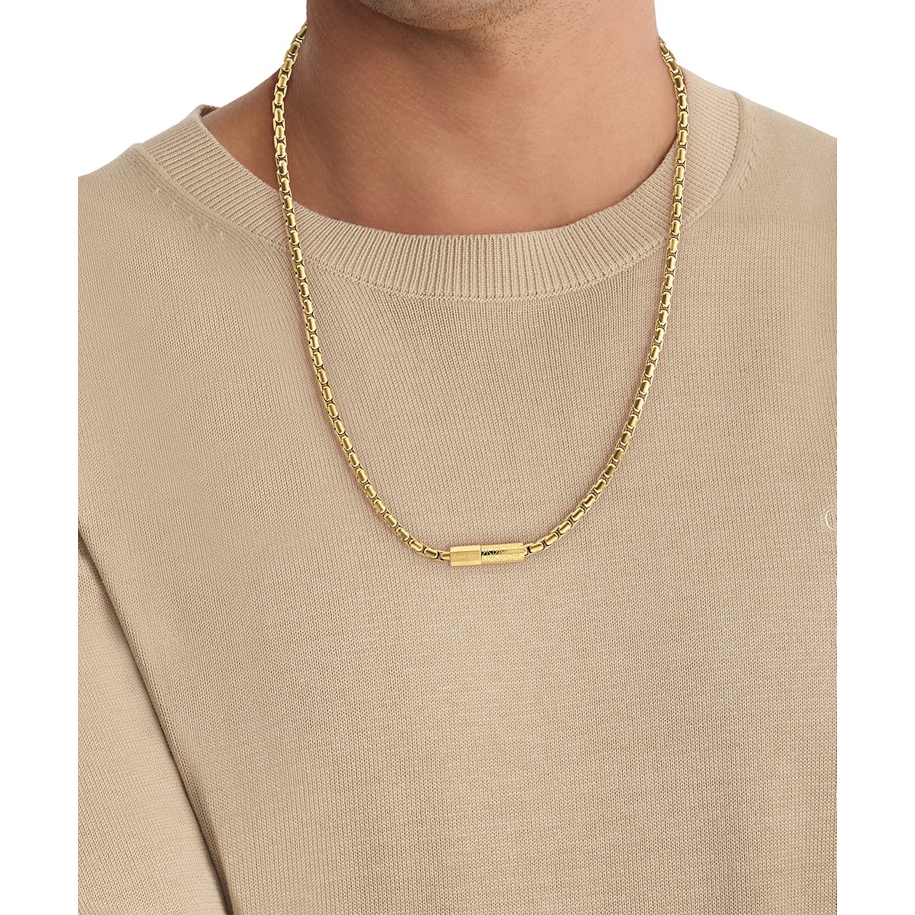 Een gouden Calvin Klein roestvrijstalen halsketting met cilindervormige hanger wordt gedragen door een man.