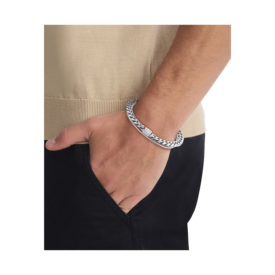 Een Calvin Klein roestvrijstalen armband, aan een pols gedragen, deels bedekt door een tas.