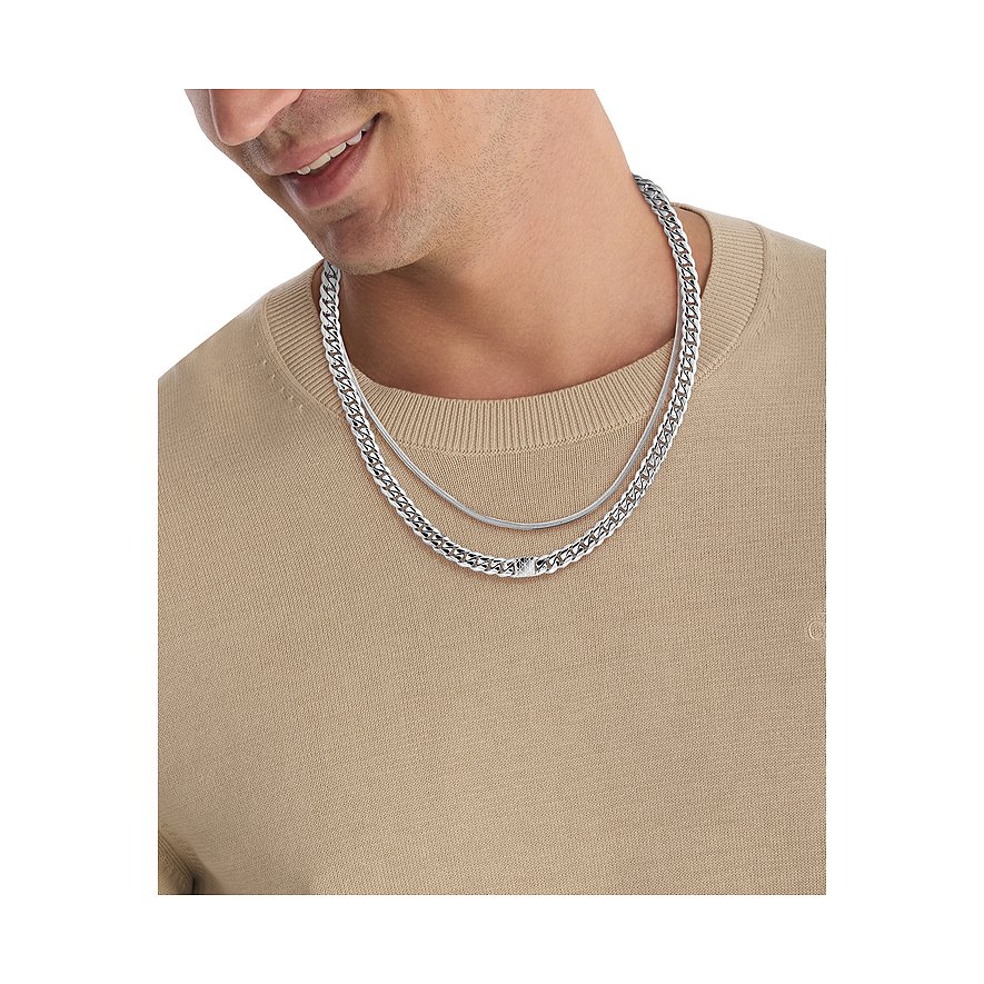 Man draagt dubbellaags Calvin Klein roestvrijstalen halsketting: een schakelketting en een figaroketting.