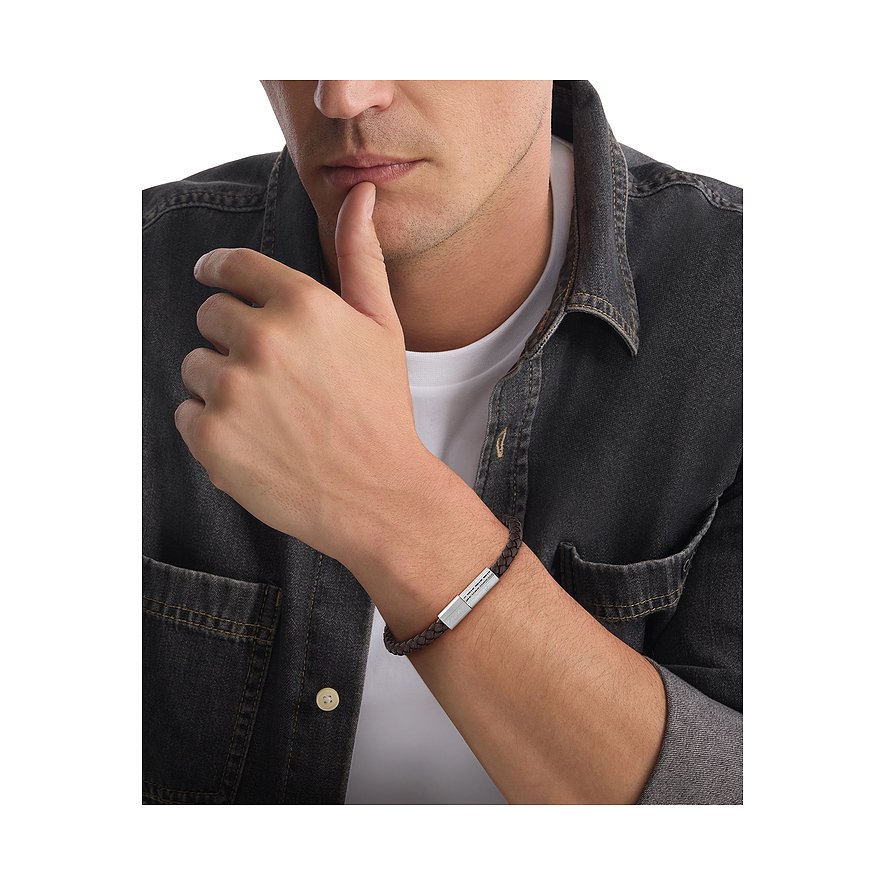 Een Calvin Klein armband van bruin gevlochten leer met een roestvrijstalen sluiting, gedragen door een man.