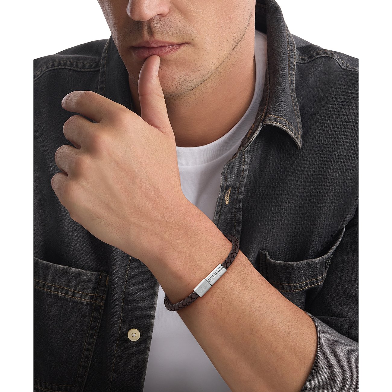 Een Calvin Klein armband van bruin gevlochten leer met een roestvrijstalen sluiting, gedragen door een man.