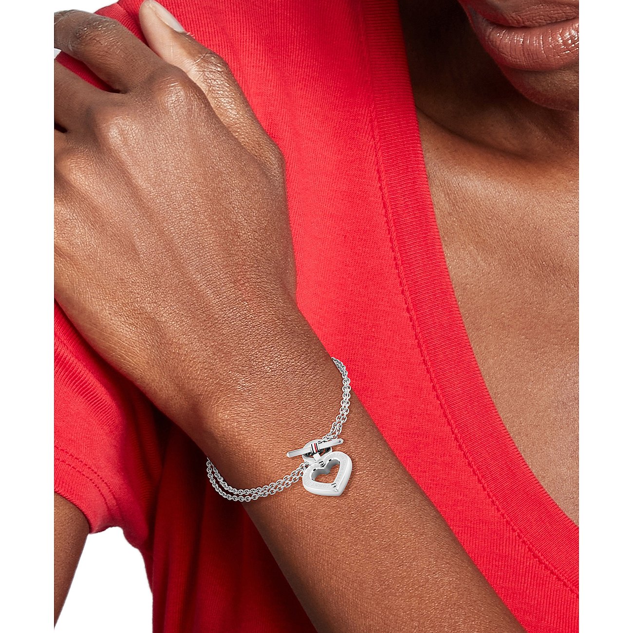 Tommy Hilfiger Armschmuck aus Edelstahl, eine silberne Gliederkette mit Herzanhänger und Knebelverschluss, auf einem Arm.