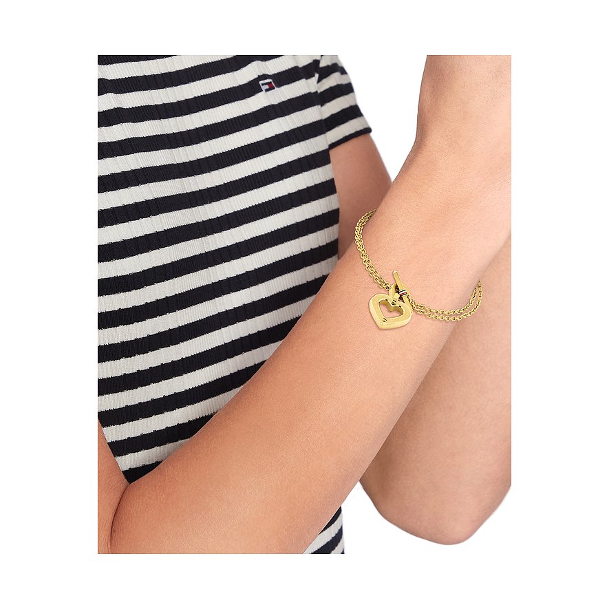 Ein Tommy Hilfiger Armschmuck aus gelb vergoldetem Edelstahl mit zwei Kettensträngen und einem Herzanhänger.