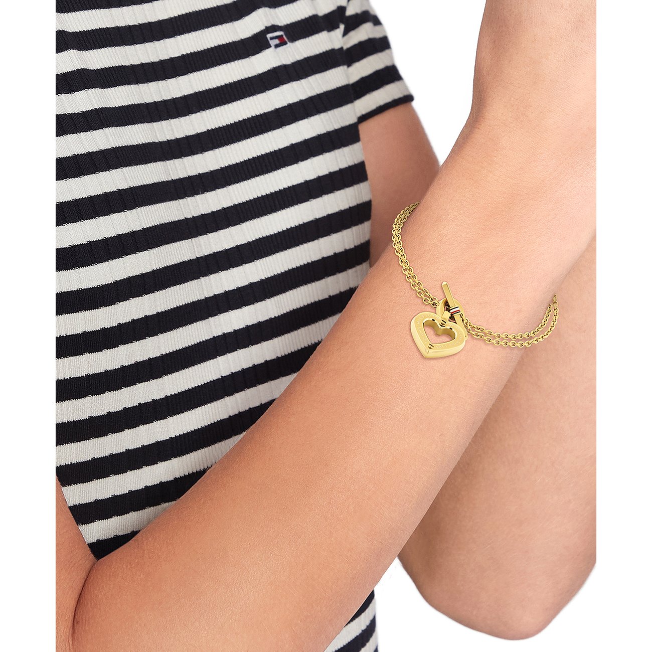 Ein Tommy Hilfiger Armschmuck aus gelb vergoldetem Edelstahl mit zwei Kettensträngen und einem Herzanhänger.