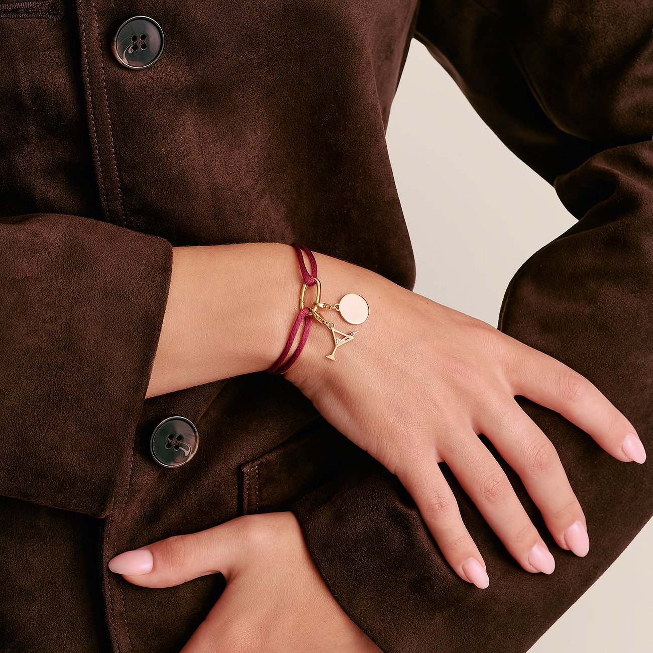 Primo piano di un bracciale Thomas Sabo in argento con nastro tessile marrone-rossastro e ciondolo a bicchiere da cocktail.