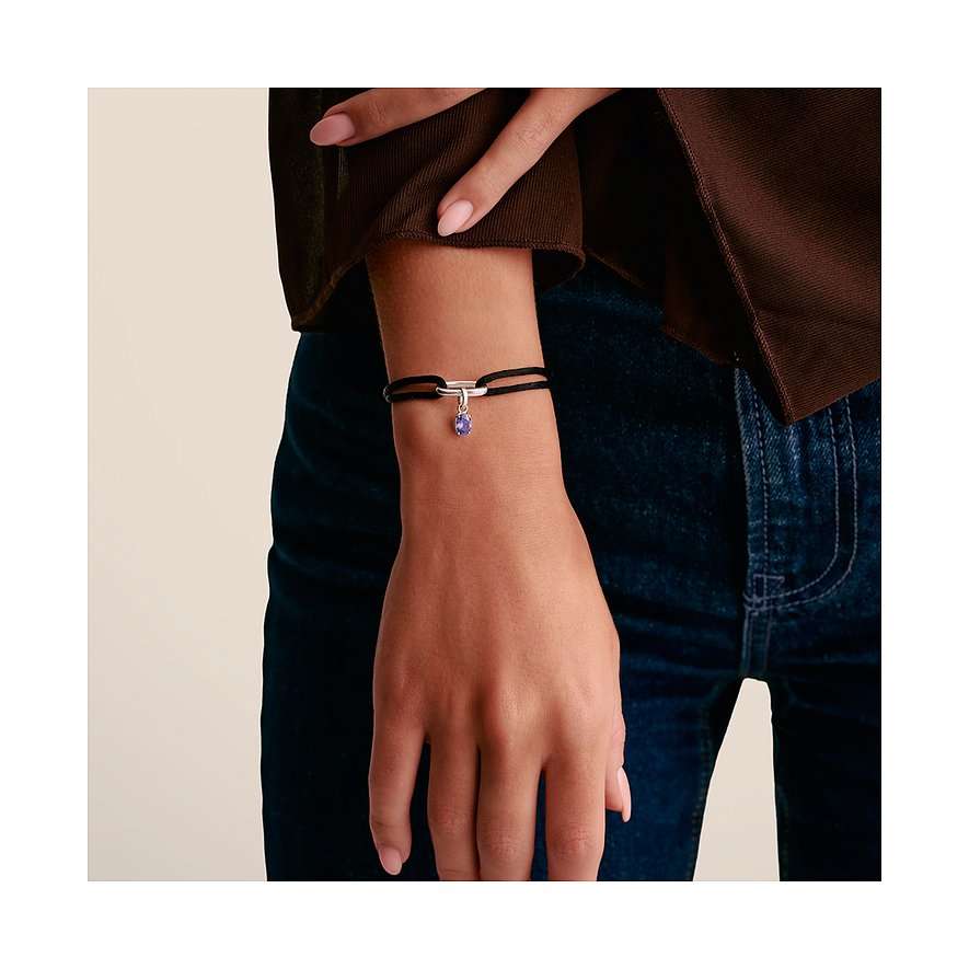 Braccio di donna con bracciale Thomas Sabo: nastro nero, chiusura argento e ciondolo pietra viola.