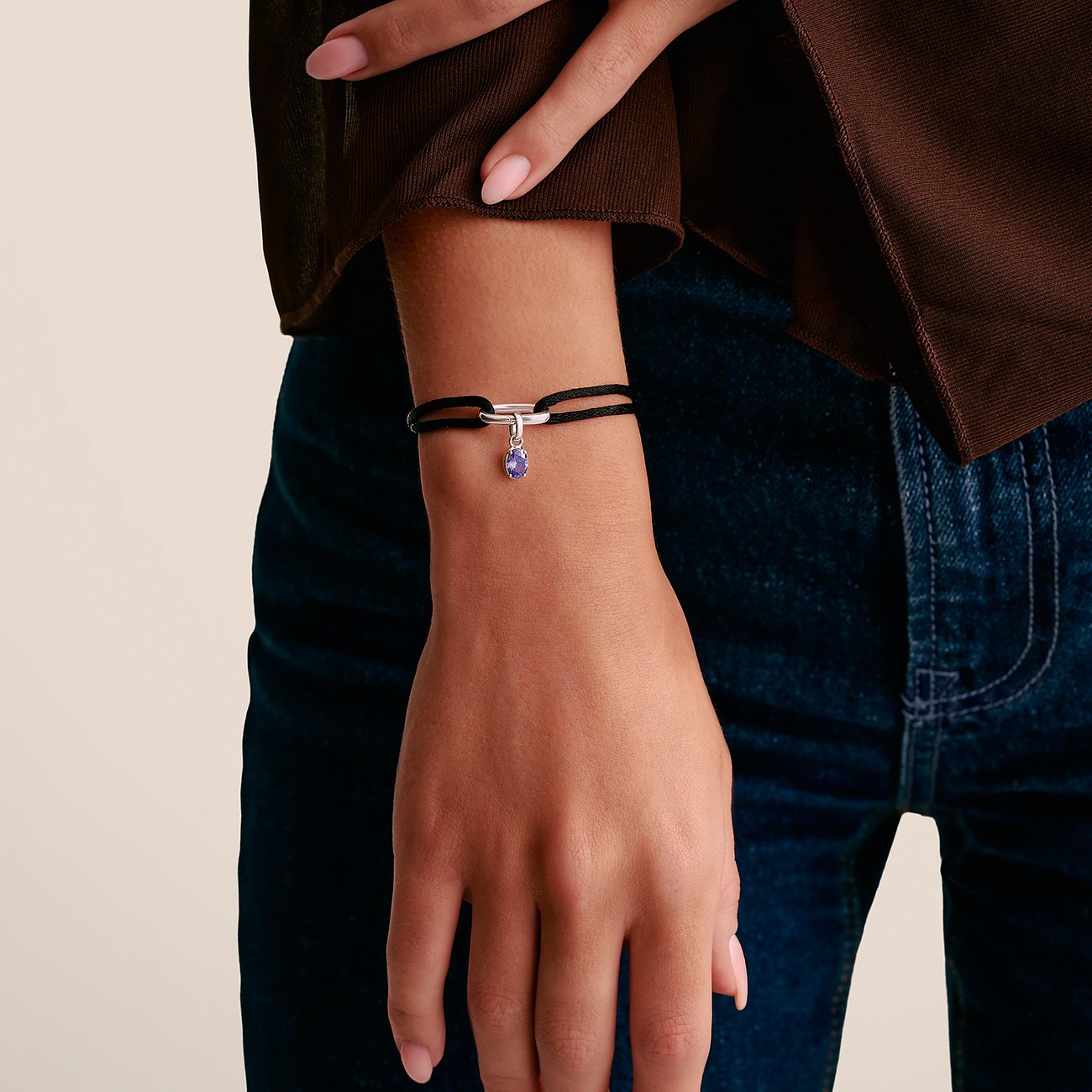 Braccio di donna con bracciale Thomas Sabo: nastro nero, chiusura argento e ciondolo pietra viola.