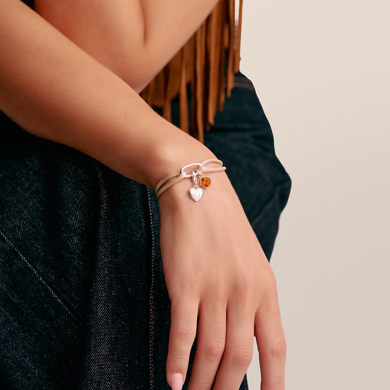 Bracciale Thomas Sabo in argento al polso con pendente a cuore e charm arancione.