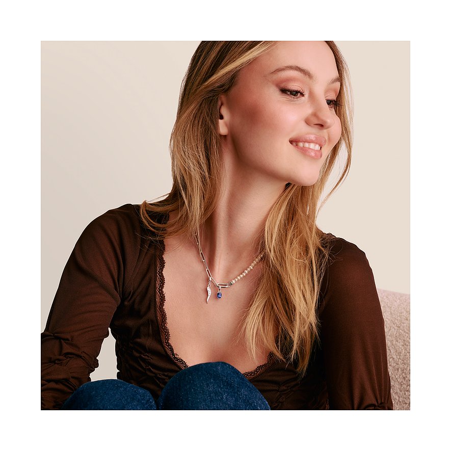 Una donna indossa una collana Thomas Sabo argento con un ciondolo in vetro blu e un altro ciondolo.