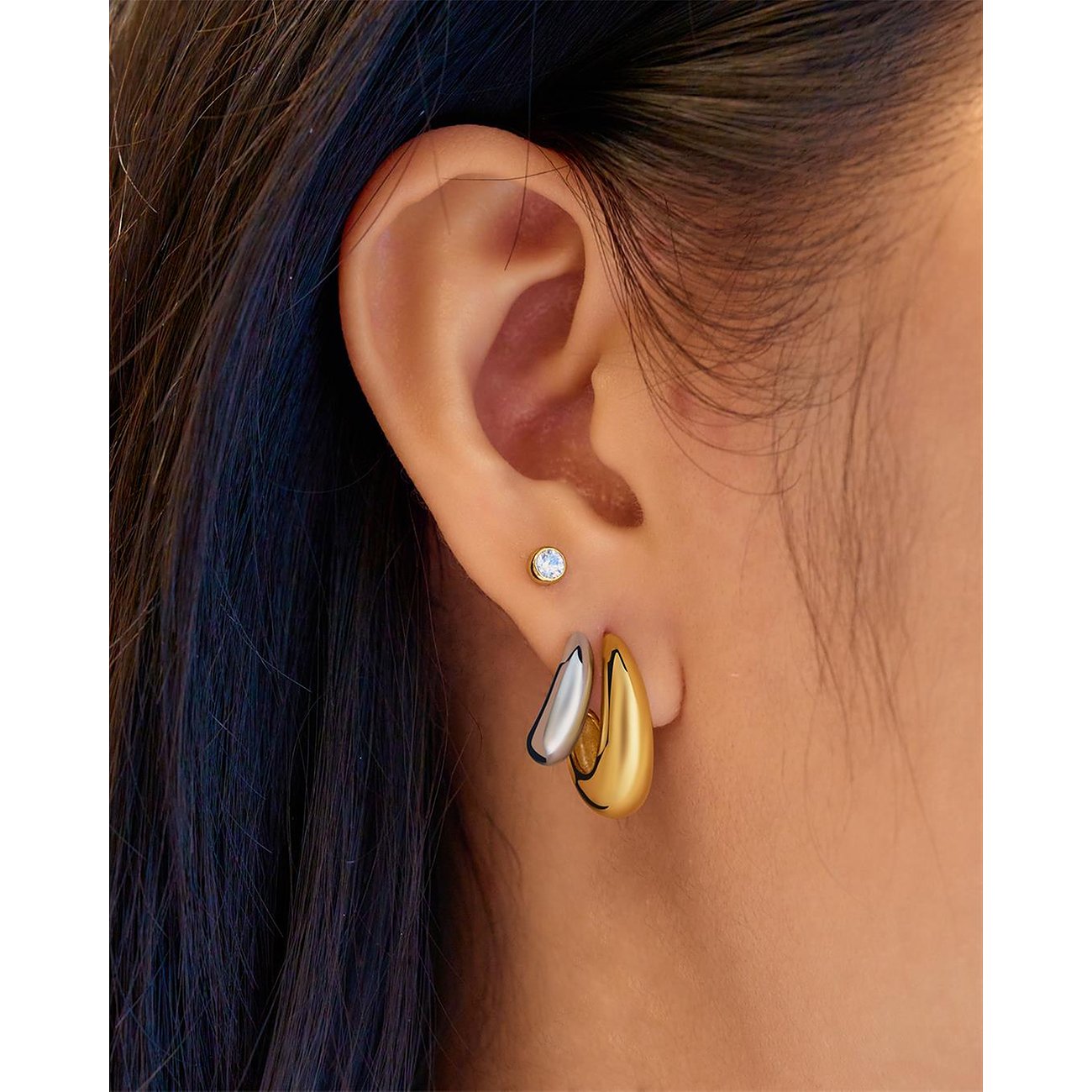 Nahaufnahme eines Ohres, das zwei Ania Haie Ohrringe trägt: einen goldenen Ohrring und einen silbernen Ohrring.