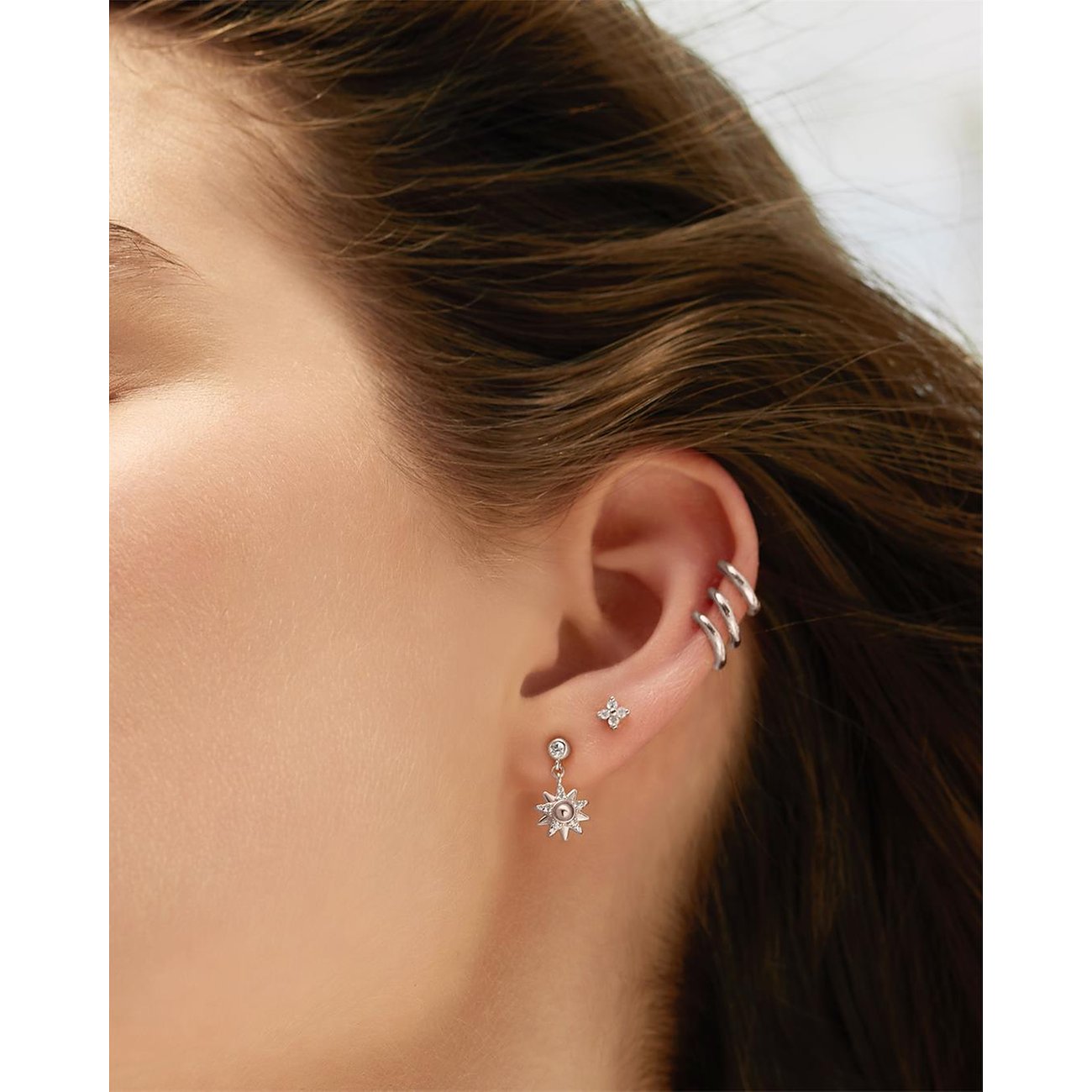 Nærbillede af et øre med Ania Haie øresmykker i 925 sterlingsølv med zirkonia-farvede sten og ear cuffs.