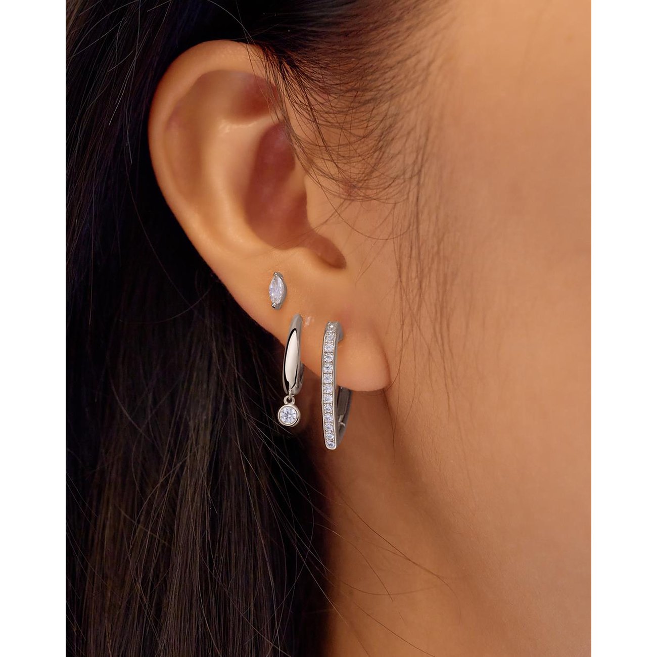 Drei Ania Haie Ohrschmuckstücke aus Silber mit Zirkonia-Farbsteinen am Ohr, darunter ein Ohrstecker in Navette-Form.