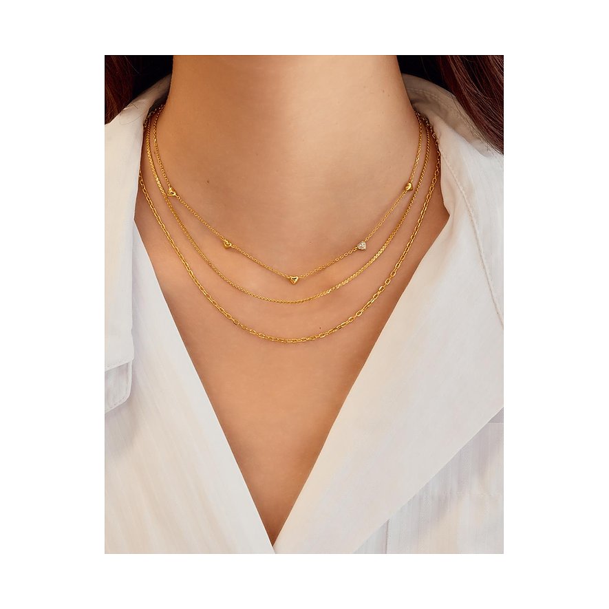 Een vrouw draagt drie goudkleurige Ania Haie kettingen van 925 zilver met zirkonia-gekleurde stenen en hart-hangers.