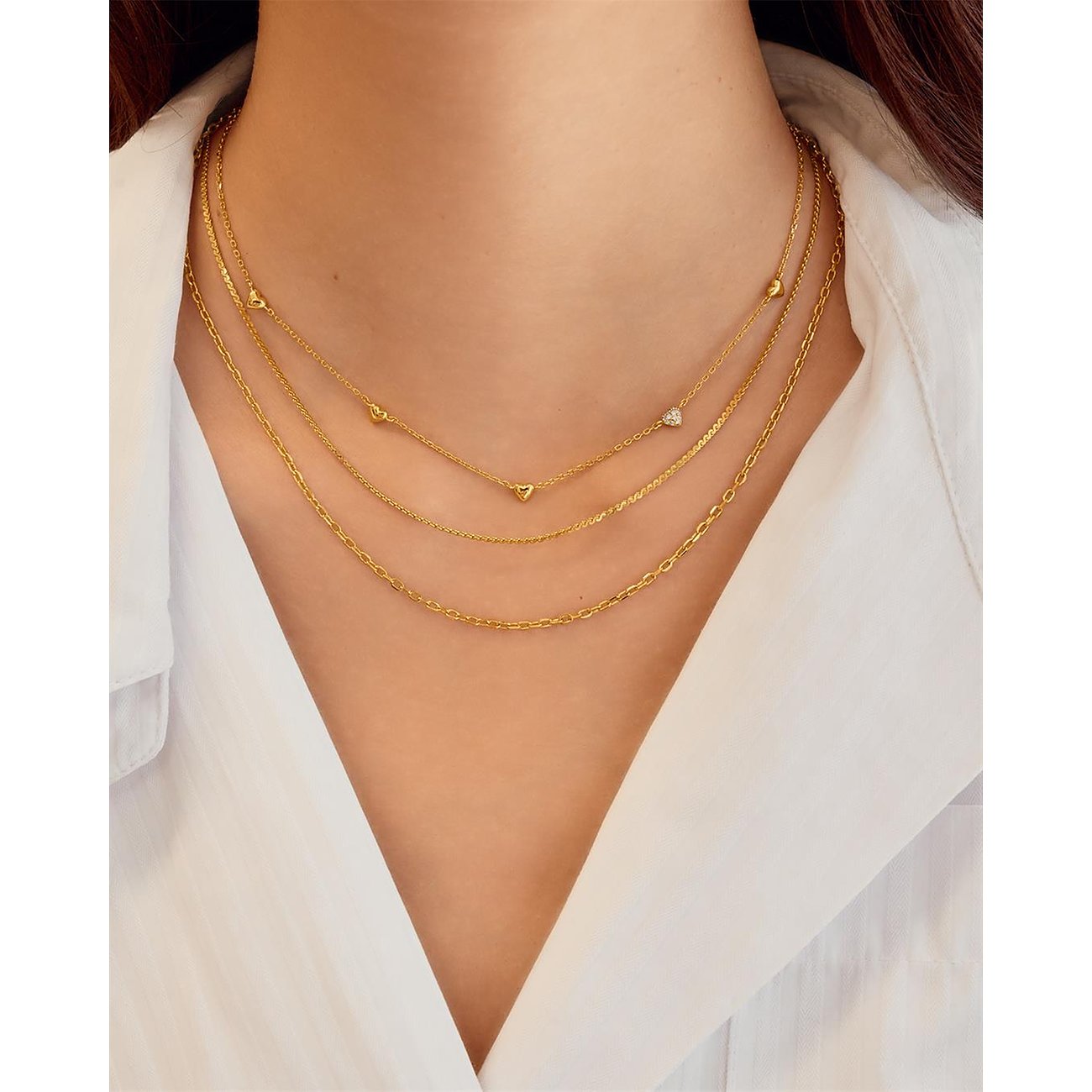 Een vrouw draagt drie goudkleurige Ania Haie kettingen van 925 zilver met zirkonia-gekleurde stenen en hart-hangers.