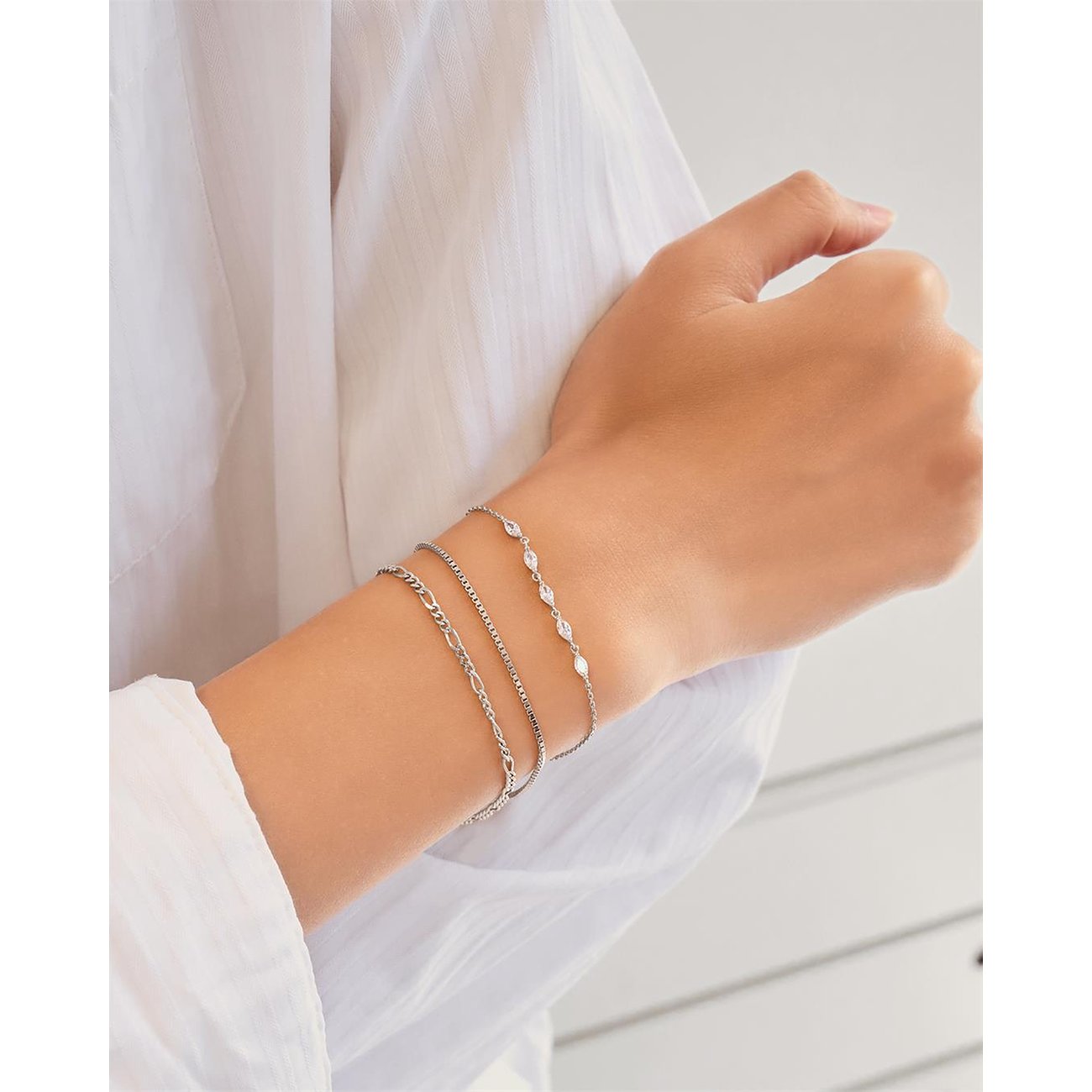 Drie Ania Haie 925 sterling zilveren armbanden om de pols, één met langwerpige zirkonia steentjes.