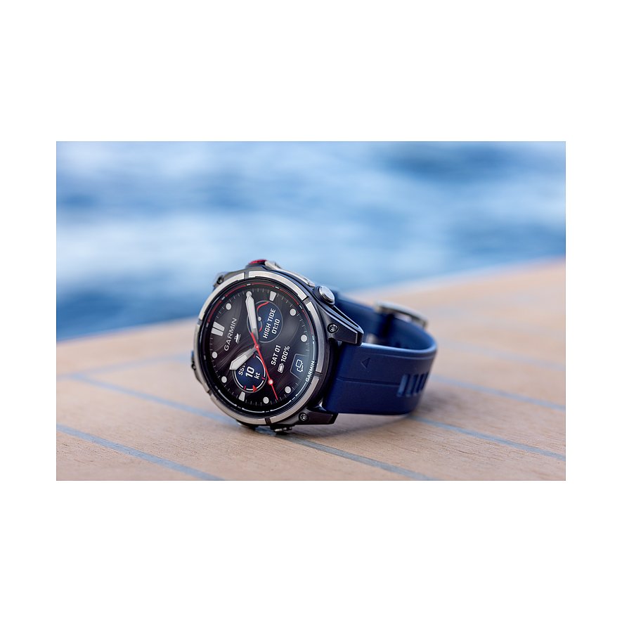 Nahaufnahme einer Garmin Smartwatch aus Metall mit dunkelblauem Armband, die auf einem Holzdeck liegt.