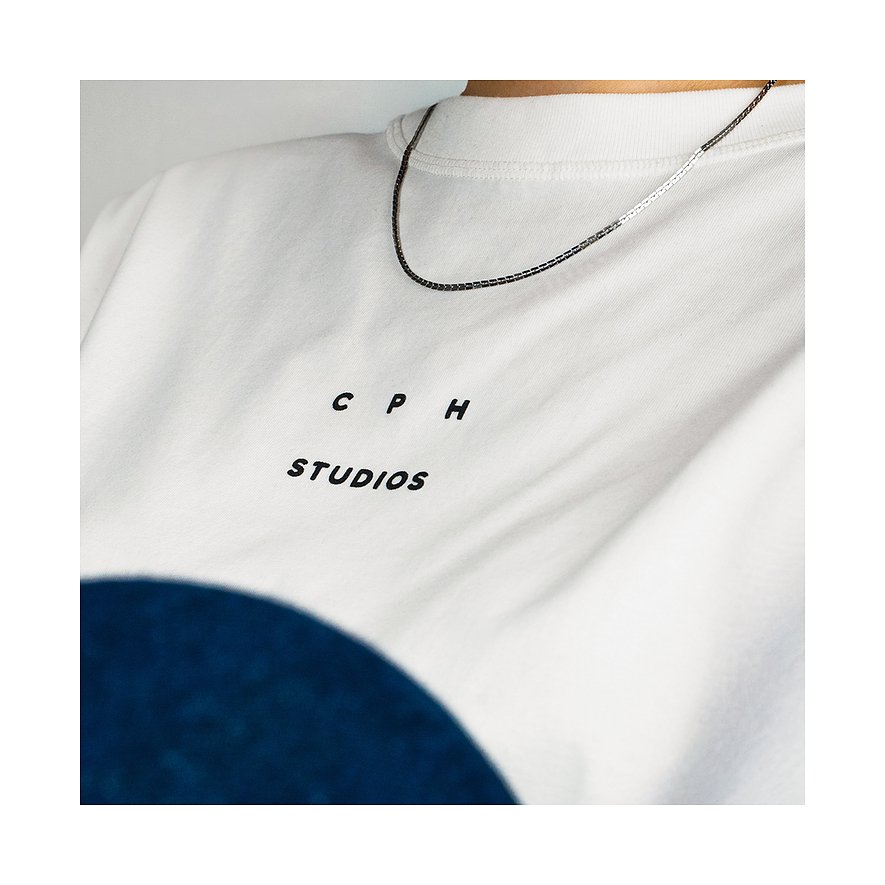 Ein Copenhagen Studios Halsschmuck aus Edelstahl, eine silberfarbene Kette, liegt auf einem weißen T-Shirt.