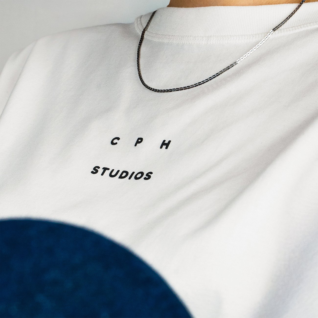 Ein Copenhagen Studios Halsschmuck aus Edelstahl, eine silberfarbene Kette, liegt auf einem weißen T-Shirt.