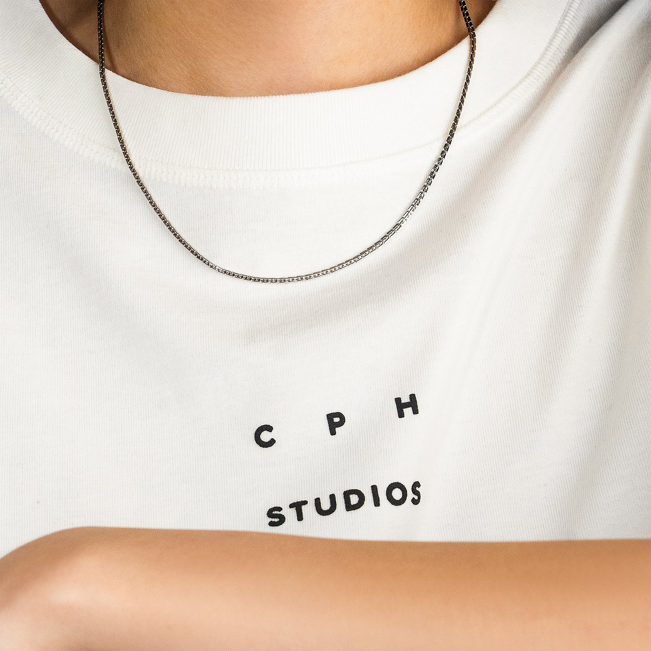 Eine graue Kette aus Edelstahl von Copenhagen Studios liegt auf einem weißen T-Shirt mit dem Aufdruck 