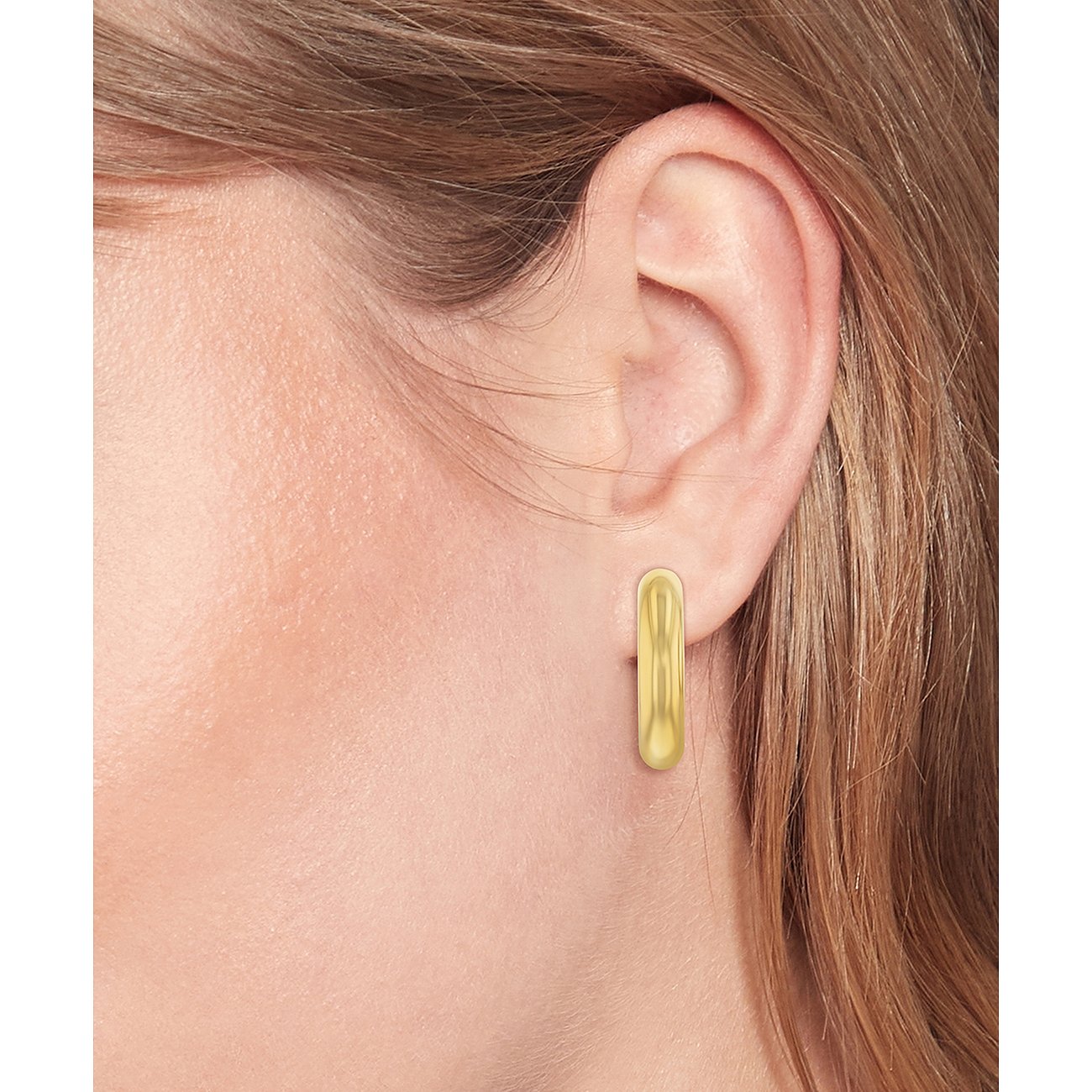 Tommy Hilfiger goldener Ohrring aus Edelstahl am Ohr einer Person, der wie eine längliche, glänzende Kapsel geformt ist.