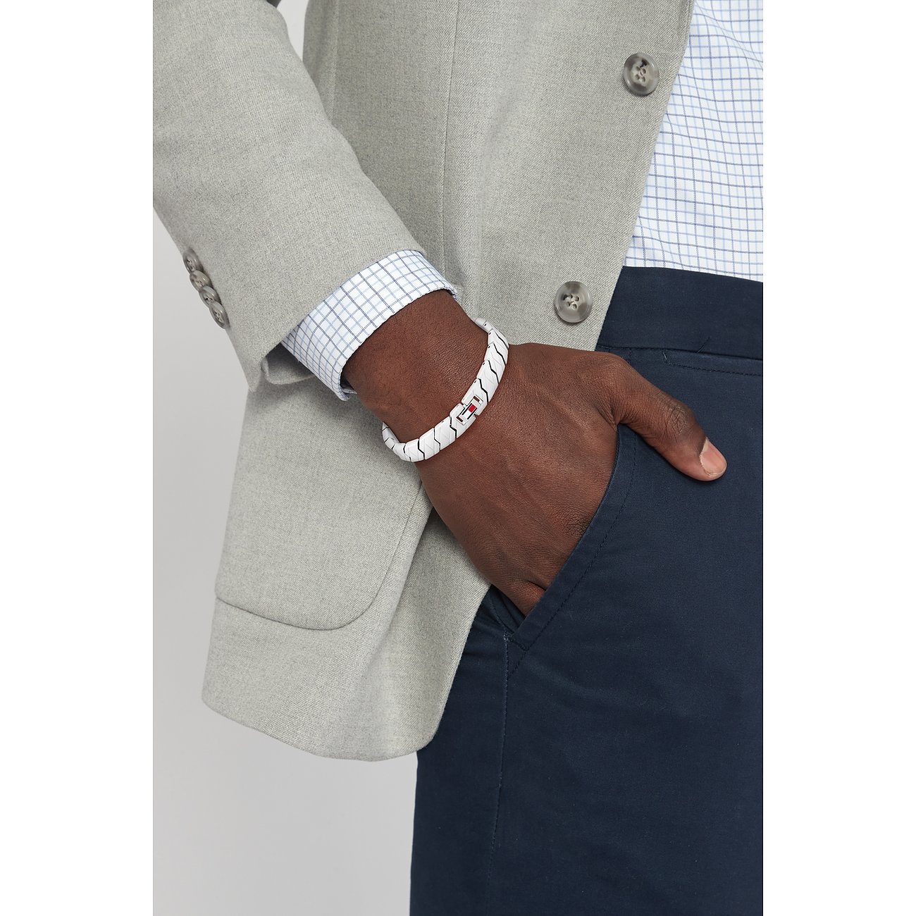 Am Handgelenk eines Mannes sitzt ein weißes Tommy Hilfiger Armband aus Edelstahl mit rotem, weißem und blauem Streifen.