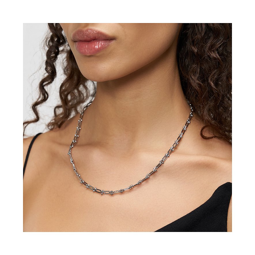 Une femme porte un collier Liebeskind en acier inoxydable avec de fins maillons en U ornés de petites perles.