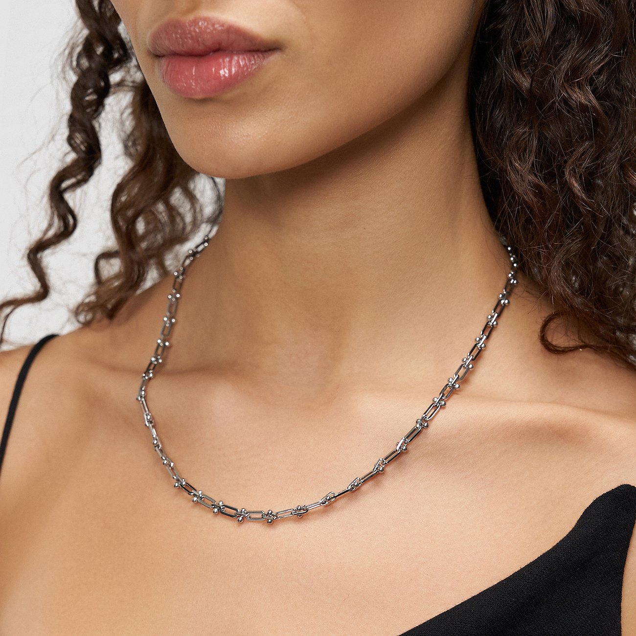 Une femme porte un collier Liebeskind en acier inoxydable avec de fins maillons en U ornés de petites perles.