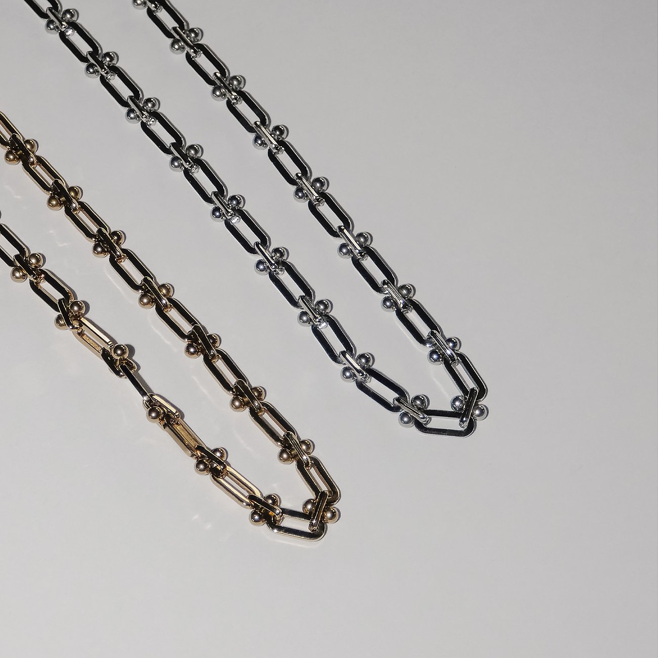 Två Liebeskind halsband i rostfritt stål, ett i guld och det andra i silver, ligger bredvid varandra.