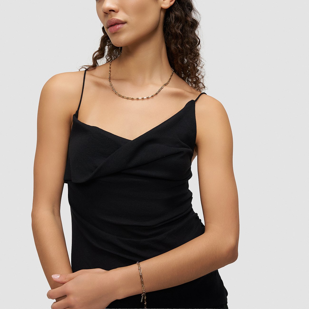 Modellen bär ett Liebeskind halsband och matchande armband i guldfärgat rostfritt stål med en svart topp.