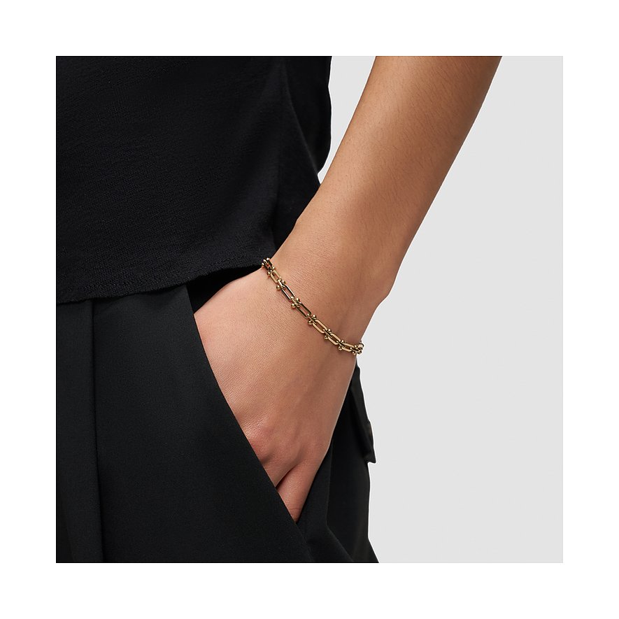 Liebeskind armbånd af guldfarvet rustfrit stål båret på et models håndled, som rækker ned i en bukselomme.