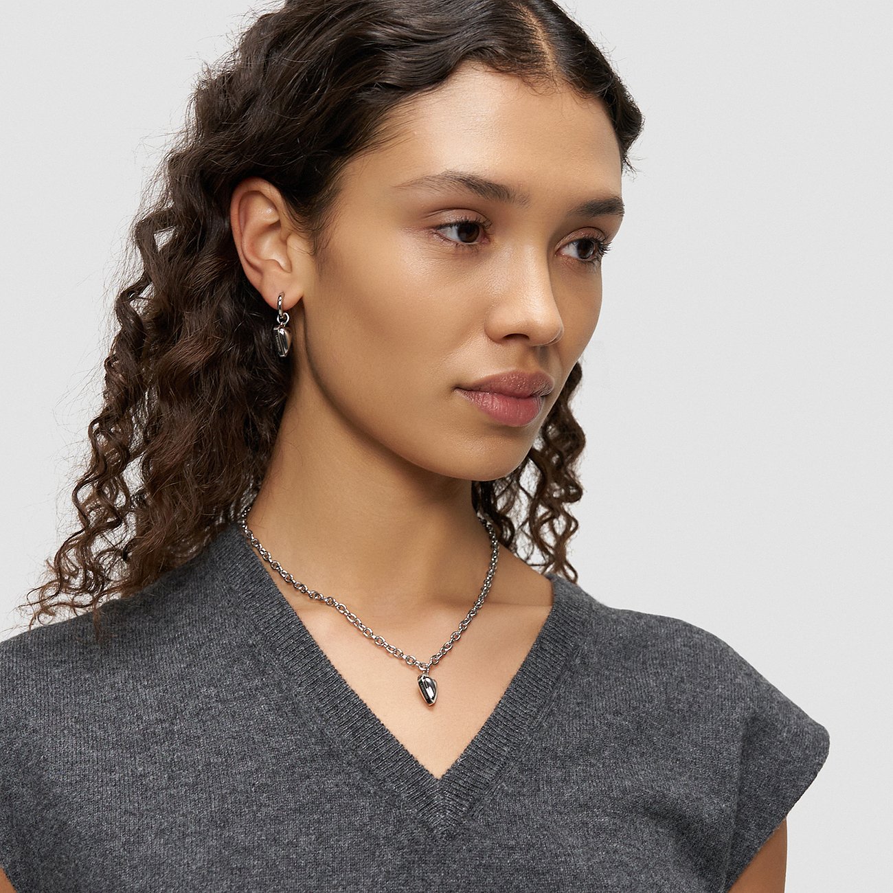 Model draagt een Liebeskind roestvrijstalen ketting en oorbellen. De ketting heeft een hanger.