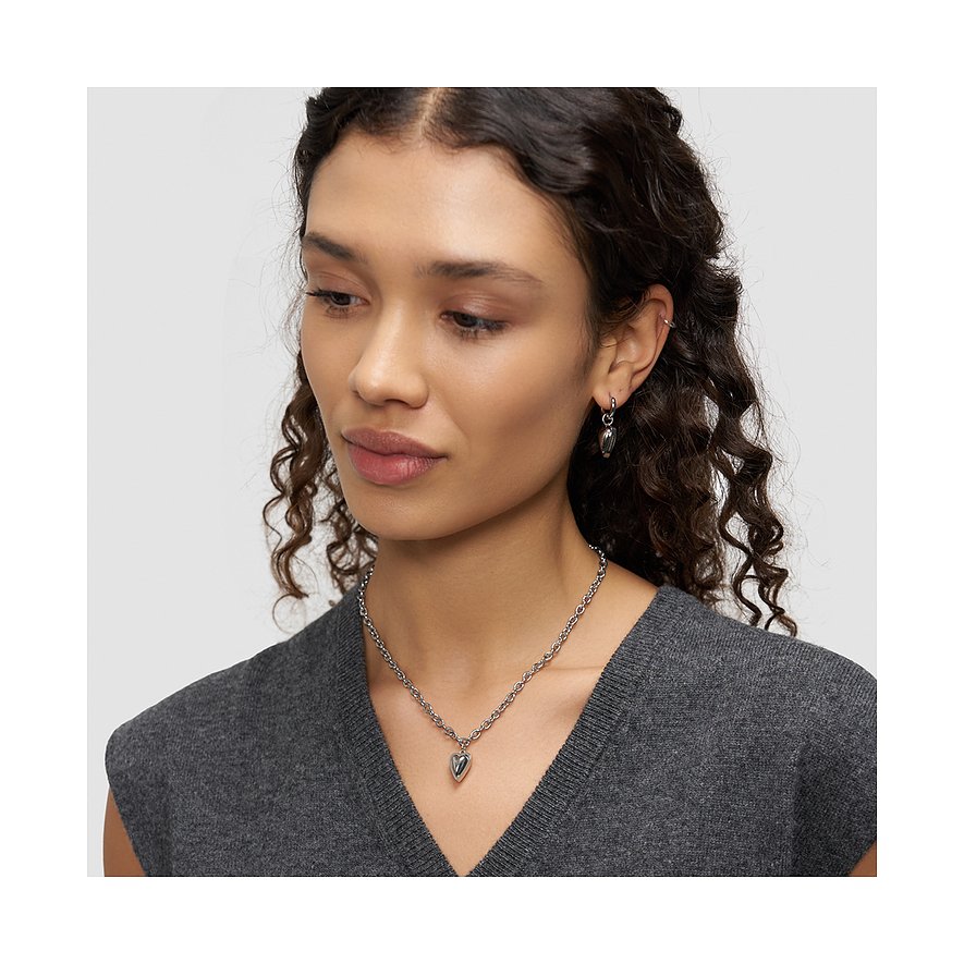 Close-up model met Liebeskind hartketting en bijpassende roestvrijstalen hartoorbellen, schuin van voren gezien.