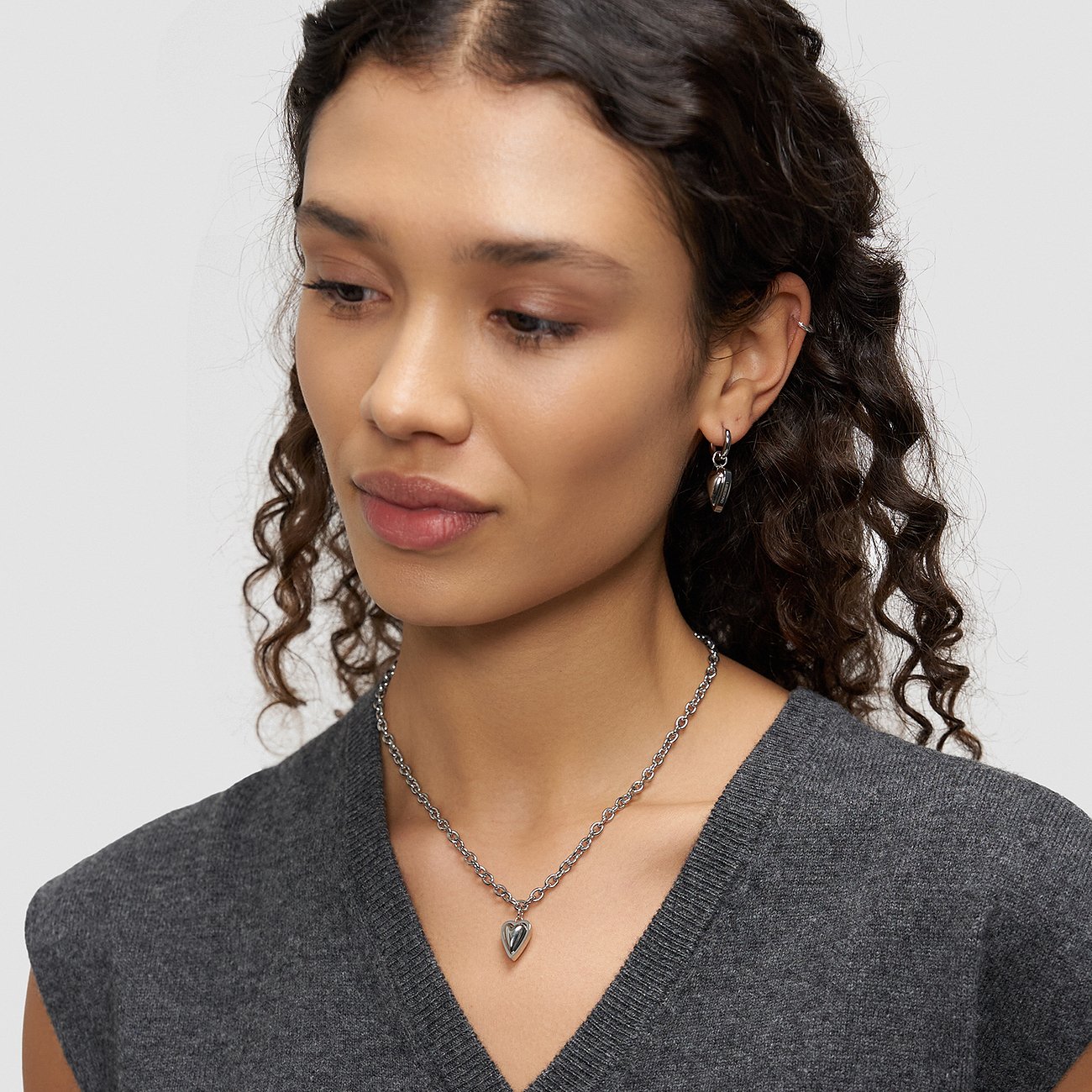 Close-up model met Liebeskind hartketting en bijpassende roestvrijstalen hartoorbellen, schuin van voren gezien.