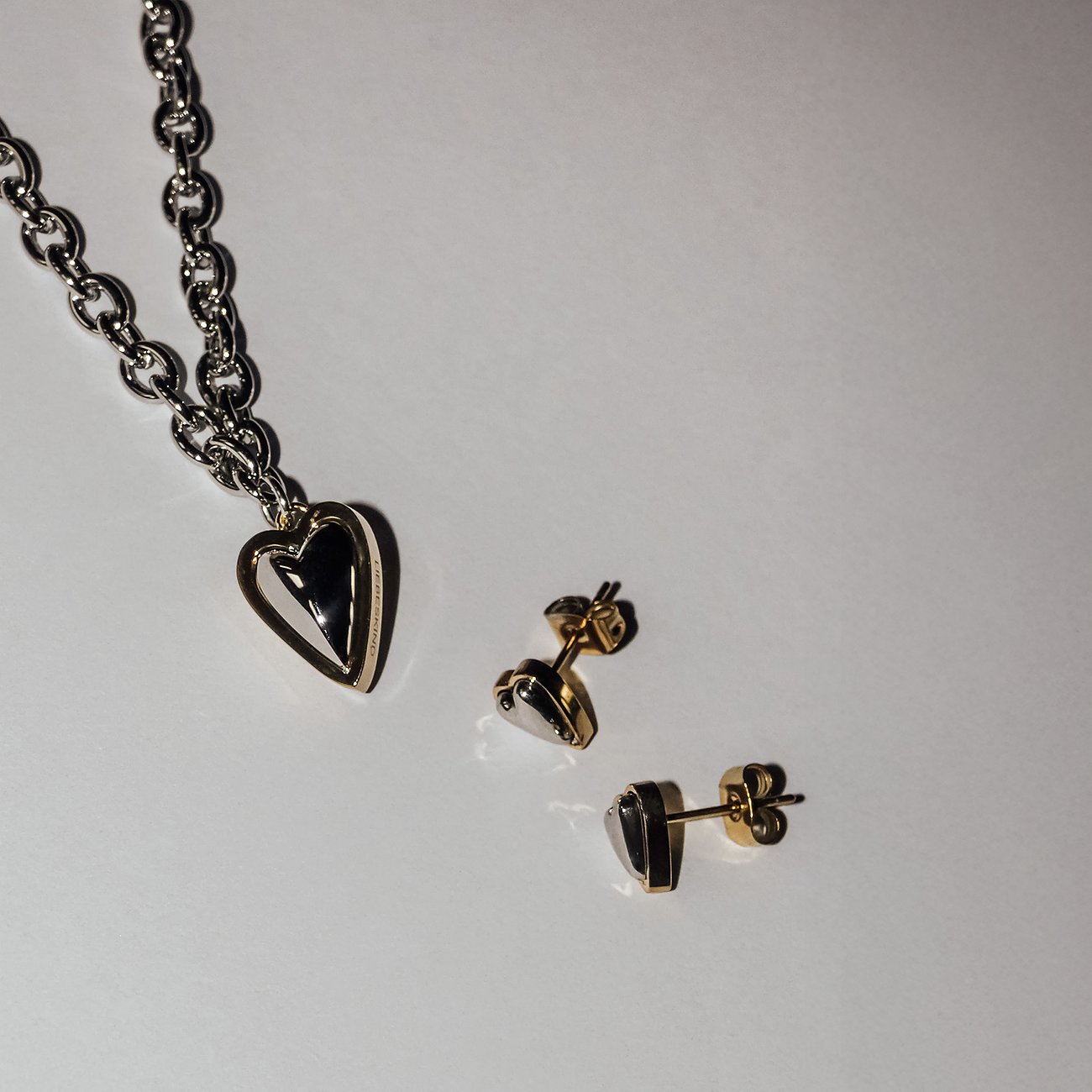 Liebeskind collier van goud- en zilverkleurig roestvrij staal met een hartvormige hanger en bijpassende oorknopjes.