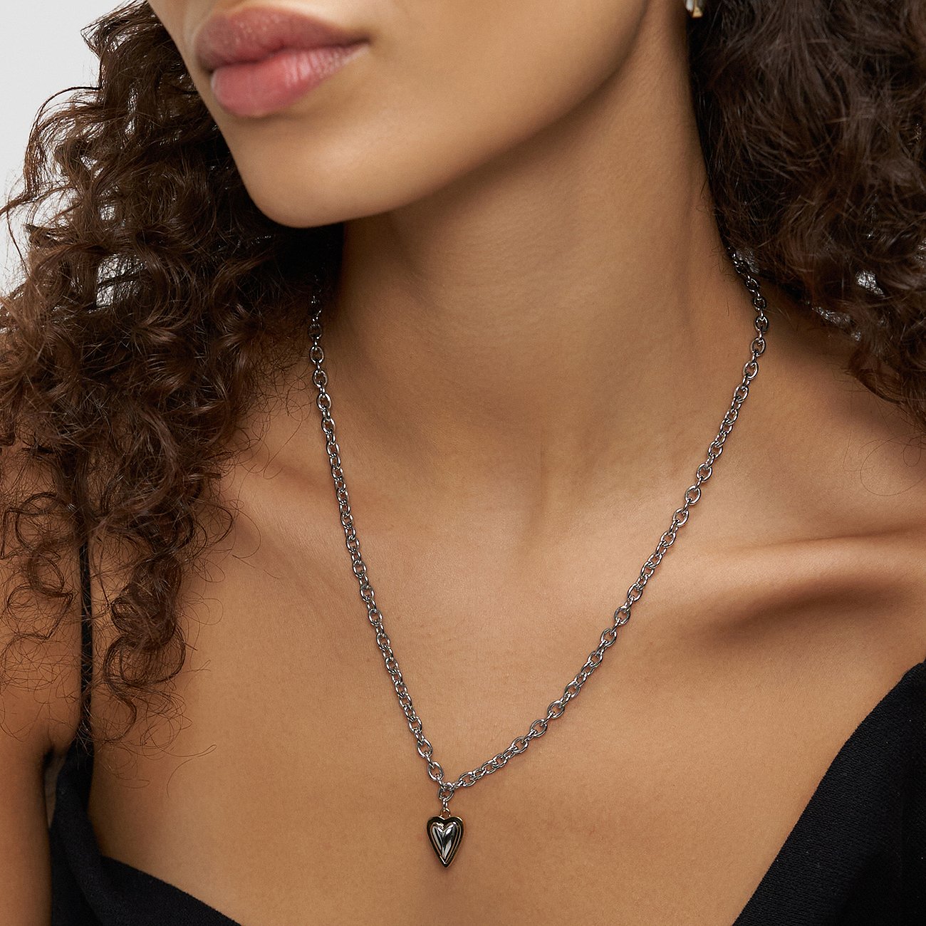 Een vrouw draagt een lange Liebeskind roestvrijstalen ketting met een glanzende hartvormige hanger.