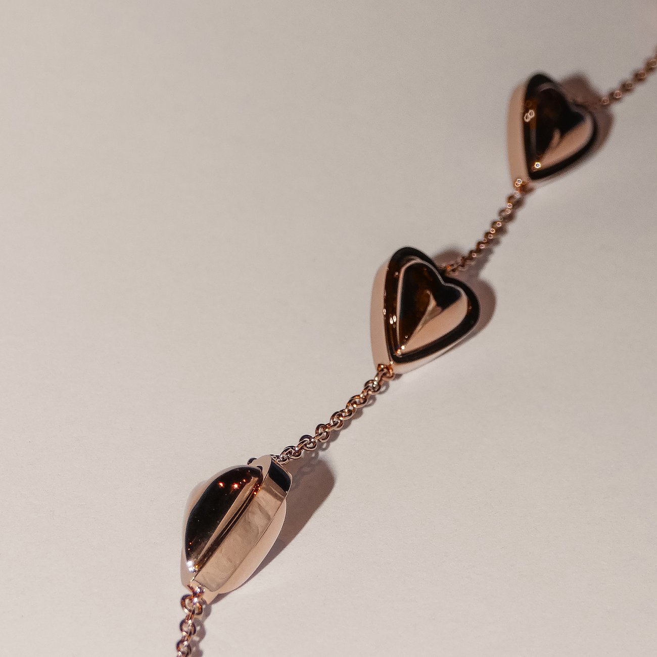 Close-up van een roségouden Liebeskind roestvrijstalen ketting met drie hartvormige hangers op witte achtergrond.