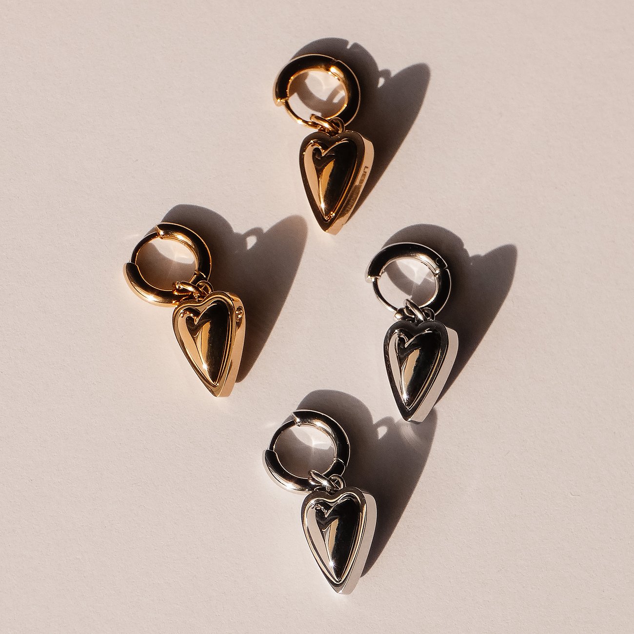 Ein Set aus Liebeskind Ohrringen mit zwei goldfarbenen und zwei silberfarbenen Herz-Anhängern aus Edelstahl.